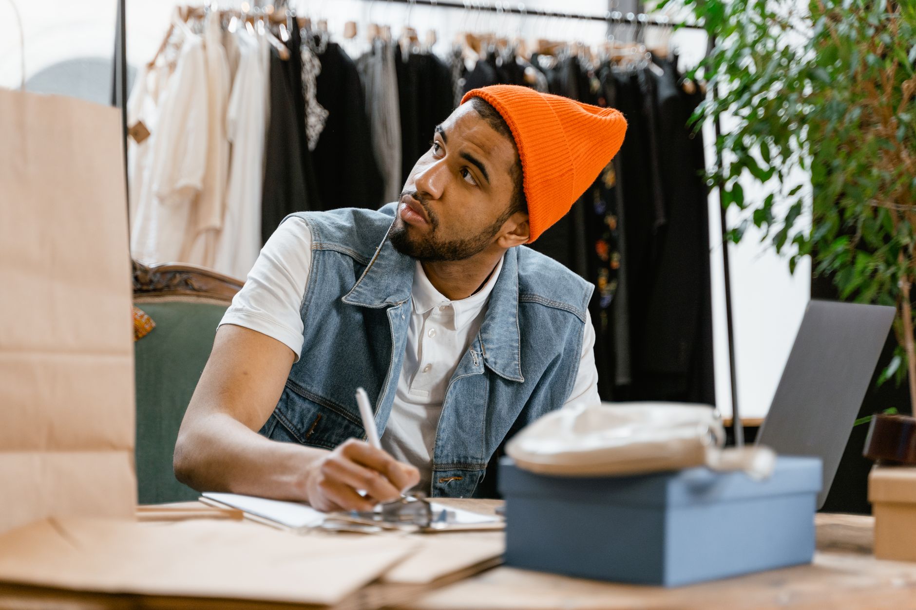 Man in bright beanie writing at a table in a boutique clothing store.